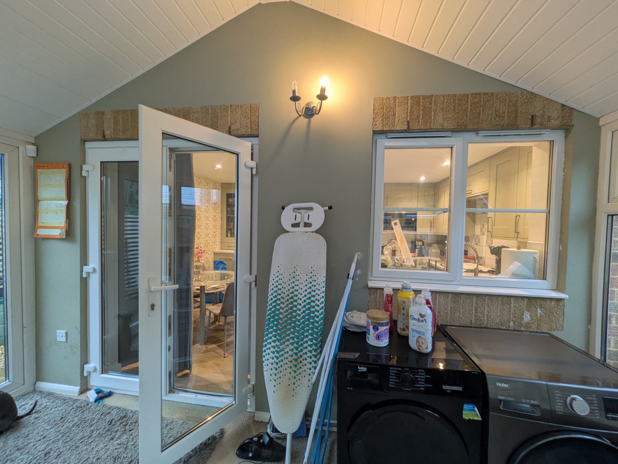 Conservatory before renovation with exposed washing machine and tumble dryer, dated finishes and poor lighting
