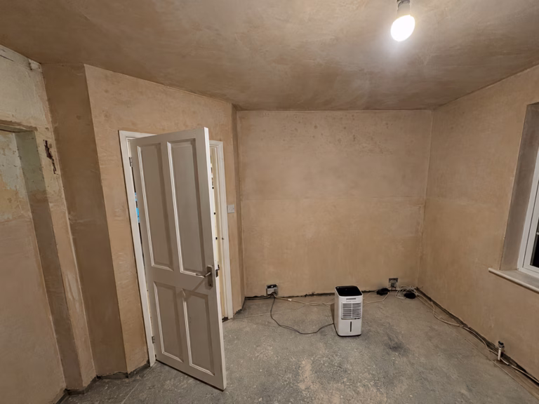 Living room before renovation in Oxshott with stripped walls, unfinished floor and preparation works underway.