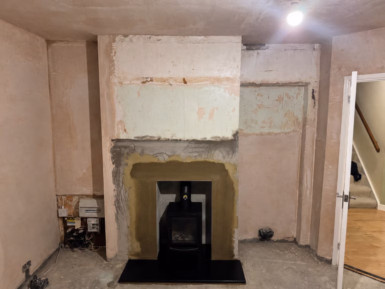 Unfinished living room in Oxshott before refurbishment, showing fireplace wall, bare plaster surfaces and exposed services.