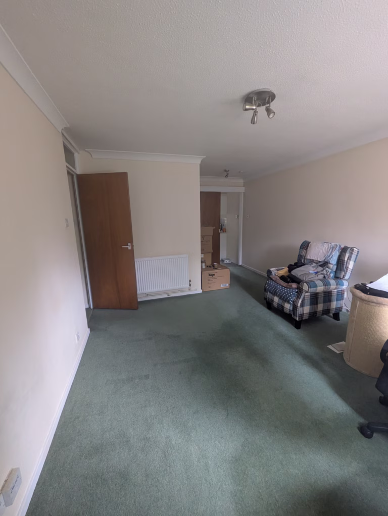 Living room before refurbishment in Guildford flat showing dated carpet, original décor, and older finishes prior to flooring replacement, wall panelling, and complete redecoration.
